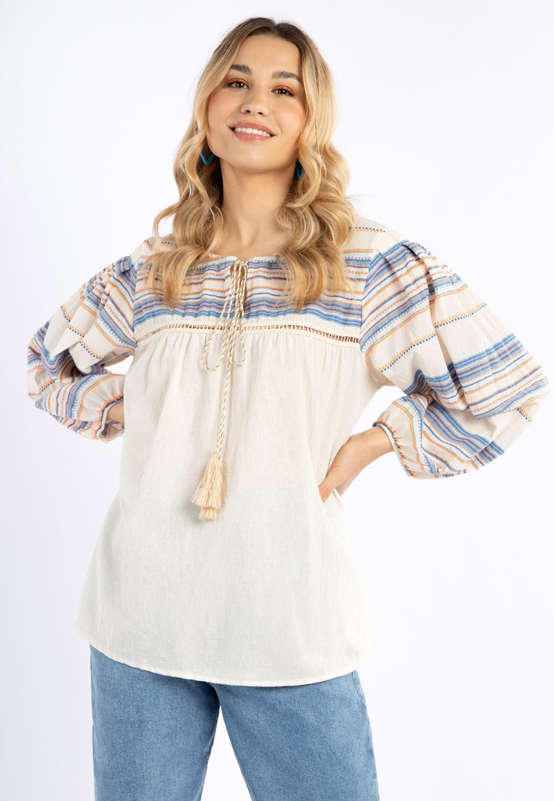 Blusa bianca con maniche a sbuffo colorate a righe. Presenta un collo rotondo, chiusura con fiocco e frange, e una vestibilità rilassata.