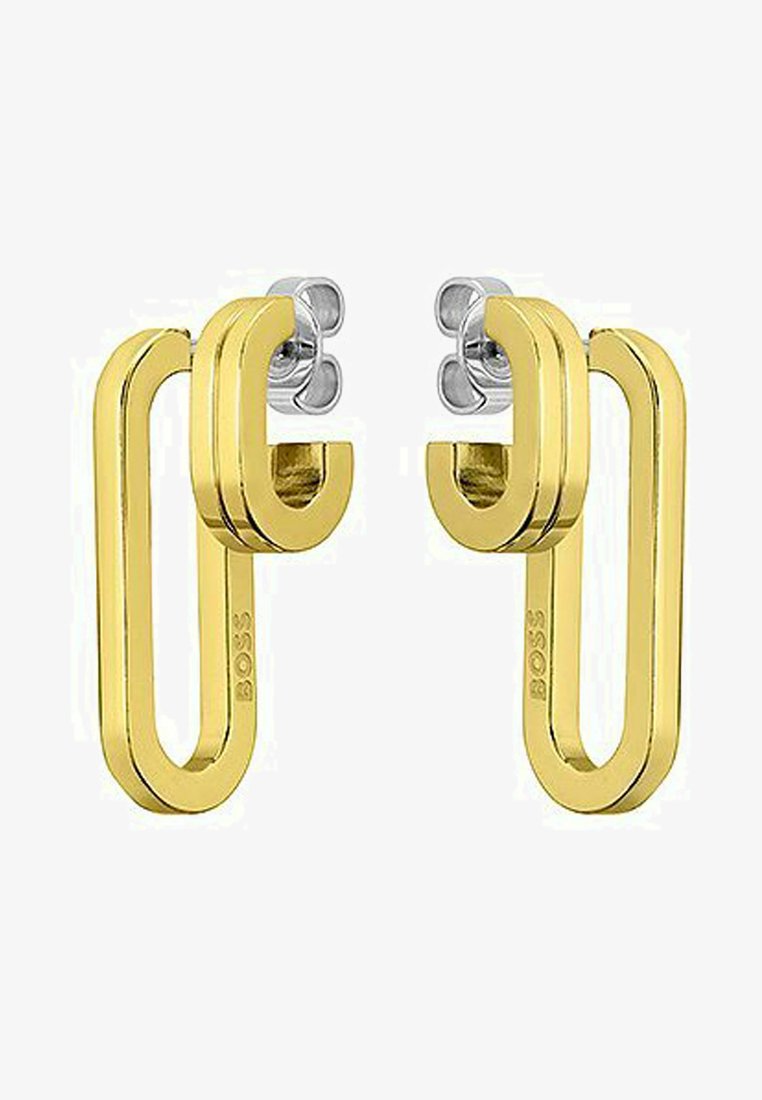 Pendientes de metal dorado con un diseño geométrico moderno que presenta una forma de bucle y acentos plateados en la parte superior. Logotipo de la marca visible.
