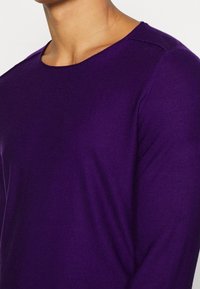 Lila tröja med en mjuk struktur, rund hals och långa ärmar. Tyget är slätt med en lätt glans, vilket säkerställer en bra passform.