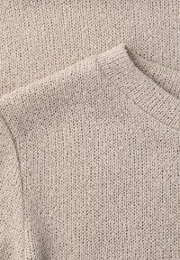 Primo piano di un maglione beige lavorato a maglia che mostra una texture dettagliata e una scollatura rotonda a coste.
