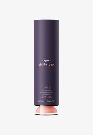 Crema pre-styling Dyson in un contenitore cilindrico viola scuro, con base trasparente e dettagli rosa chiaro. Testo: "Condizionamento ricco per capelli ricci a crespi."