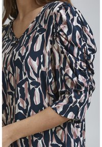 Blusa con motivo nei colori blu navy, rosa e crema. Presenta maniche a sbuffo e un design a scollo a V. Il tessuto è liscio con una texture leggera.