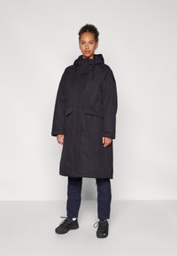 Parka lungă neagră cu glugă, cu fermoar în față, două buzunare frontale și o croială lejeră. Fabricată dintr-un material durabil, texturat.