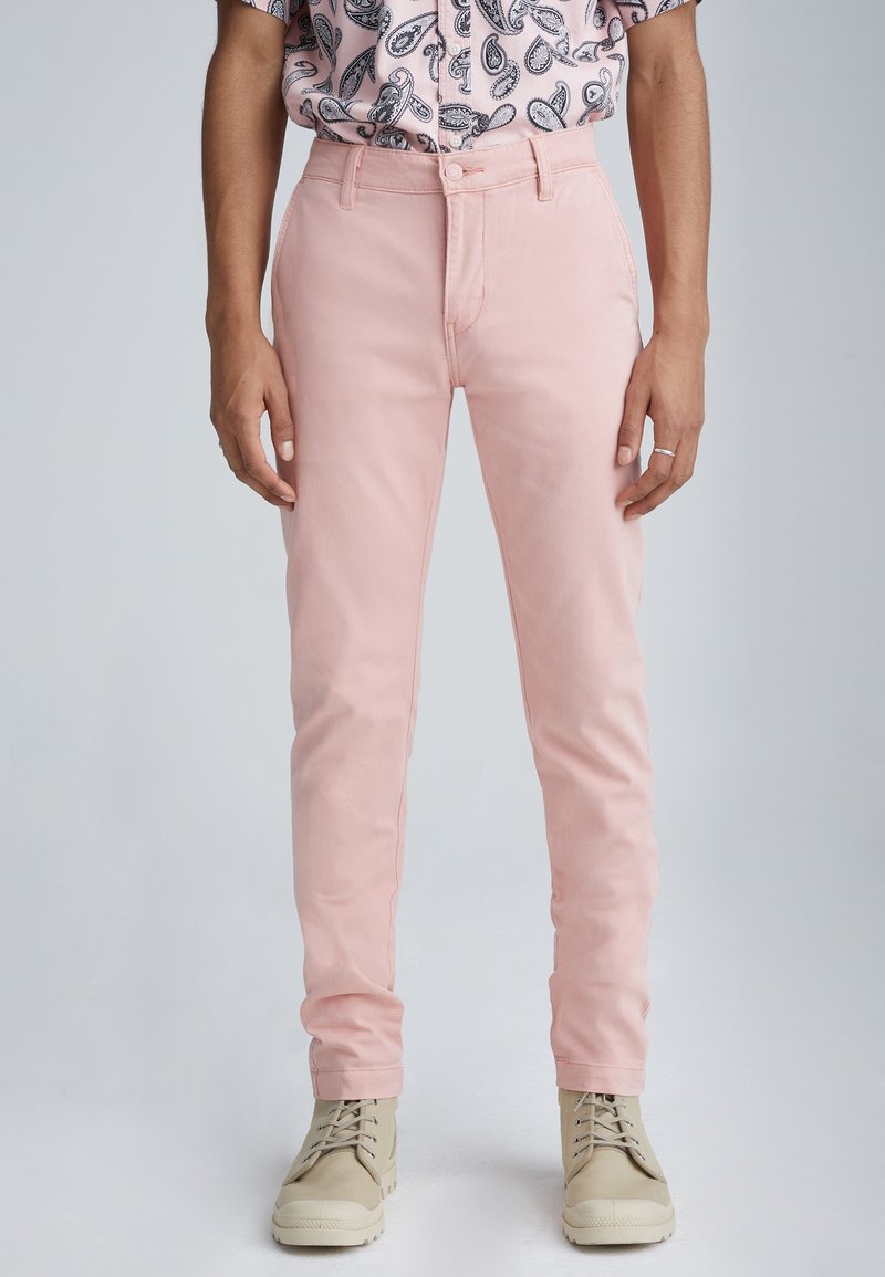 Pink cotton pants with a slim fit, featuring a classic five-pocket design and belt loops, paired with beige lace-up shoes.