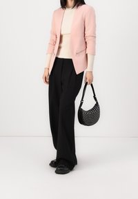Světle růžový blazer s kapsami na zip, krémový žebrovaný top, černé kalhoty se širokými nohavicemi a černá kabelka s bílými puntíky. Černé platformové boty.