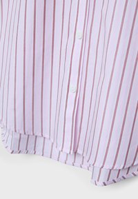 Jasnoróżmy dół koszuli z pionowymi, cienkimi czerwonymi paskami i dwoma białymi guzikami, tkanina lekko zakrzywiona i zachodząca na siebie na dole.