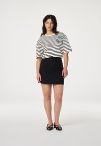 Gestreept shirt met korte mouwen in beige en zwart, met een groene grafiek. Gepaarde met een zwarte denimrok, versierd met vetersluiting.