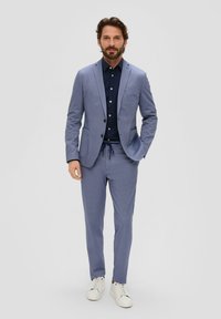 Lichtblauw pak met een subtiel patroon, gecombineerd met een marineblauw shirt. Witte sneakers maken de look compleet. Op maat gemaakt met een eigentijds ontwerp.