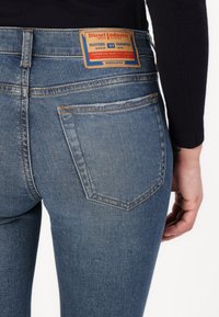 Faded blue denim jeans with a back pocket and a brown leather tag featuring brand details and stitching. Smooth texture and slim fit.