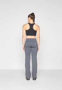 Crni skraćeni top s dizajnom racerback u kombinaciji sa sivim širokim yoga hlačama, oboje od mekanog, rastezljivog materijala. Nema značajnih uzoraka ili hardvera.