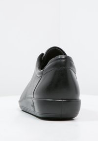 Svart lädersko med en slät yta, rund form och låg profil på yttersulan. Förstärkt häl för extra stöd.