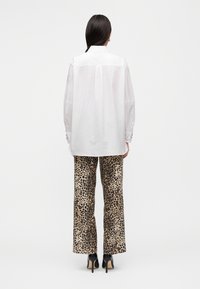 Λευκό πουκάμισο με γιακά και μακριά, ελαφρώς φουσκωτά μανίκια. Συνδυασμένο με παντελόνι καμπάνα με λεοπάρ τύπωμα και ψηλή μέση, καθώς και μαύρες γόβες.