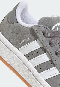 Zapatilla de ante gris con rayas de cuero blanco, suela de goma texturizada y cordones grises. Presenta la marca "CAMPUS" en el lateral.