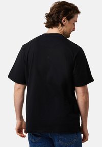 Musta puuvillapaita, jossa on lyhyet hihat ja pyöreä kaula-aukko. Takana on sileä pinta, jossa on vähän saumoja ja ei näkyviä logoja.