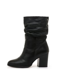 Botín de cuero negro con diseño holgado, punta redonda y tacón grueso. Marca sutil en el lateral. Textura suave en toda la superficie.