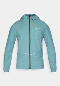 Ελαφρύ, τιρκουάζ μπουφάν με μπροστινό φερμουάρ, ρυθμιζόμενη κουκούλα και ανακλαστικές λεπτομέρειες. Έχει ελαστικές μανσέτες και αεροδυναμικό σχέδιο.