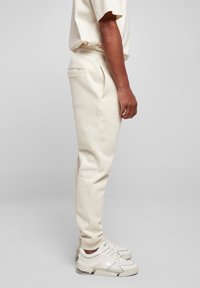 Pantalones jogger de color crema hechos de material suave, con bolsillos laterales, ajuste entallado y puños acanalados. Llevados con zapatillas blancas y grises.