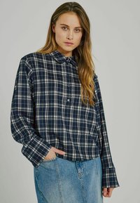 Marineblå och vit rutig skjorta med krage, långa ärmar och avspänd passform, kombinerad med ljust blå denimkjol.