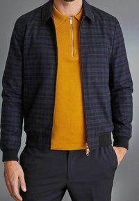 Navy checkered bomber jacket with ribbed cuffs, paired with a yellow zip-neck polo shirt, featuring a textured fabric and slim fit.