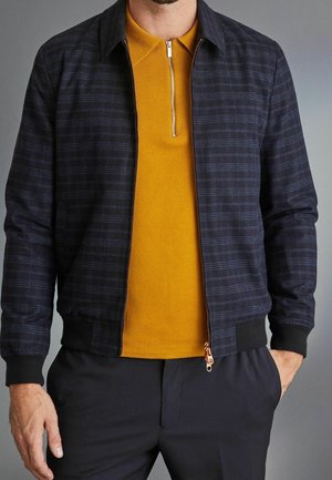 Veste bombardier à carreaux marine avec des poignets côtelés, associée à un polo jaune à col zippé, avec un tissu texturé et une coupe slim.