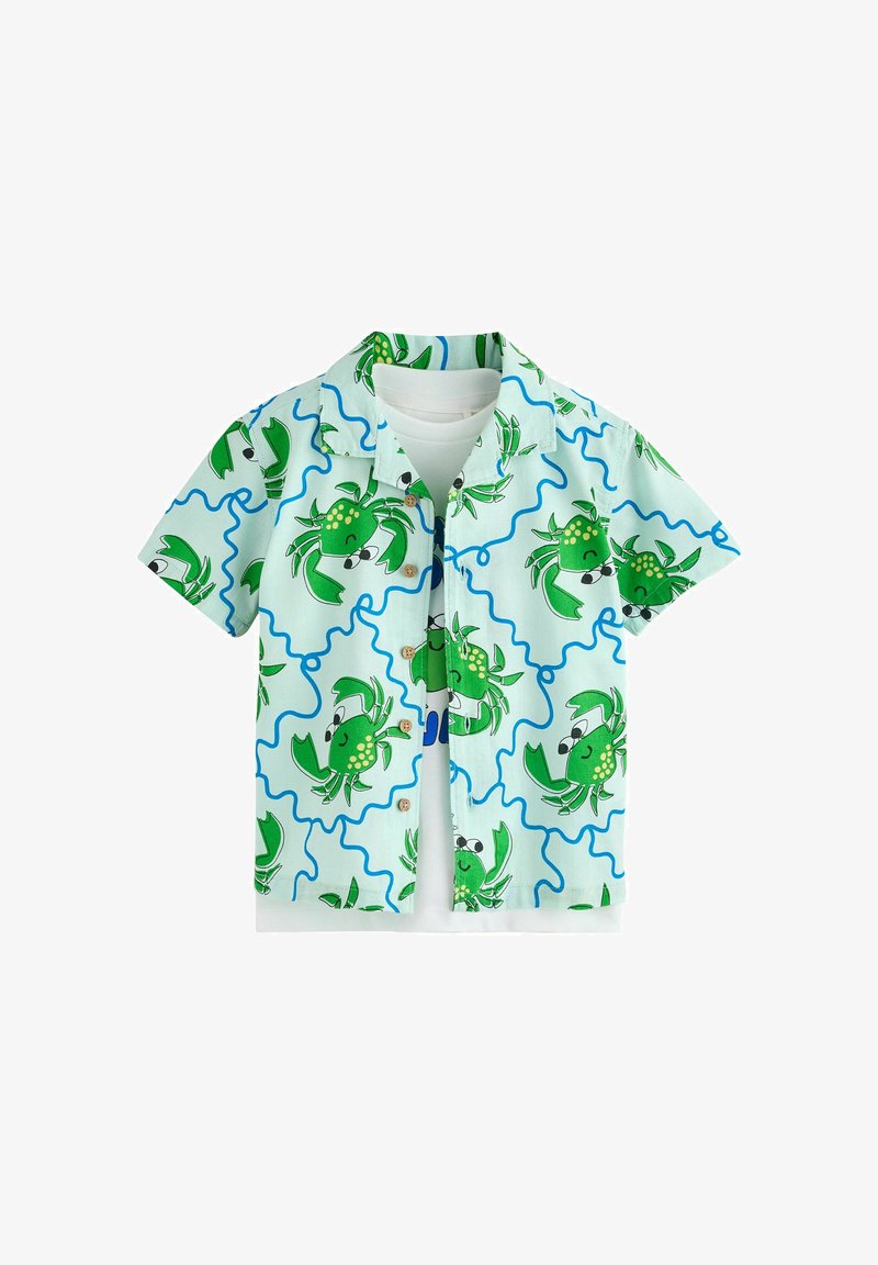 Chemise à manches courtes bleu clair avec des crabes verts dessinés en bande dessinée et des lignes ondulées bleues, superposée à un T-shirt blanc uni.