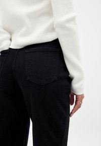 Musta denimid, millel on figuuri rõhutav disain. Omadused sisaldavad kahte tagataskut, siledat tekstuuri ja õrna puuvillast õmblustasku detaili.