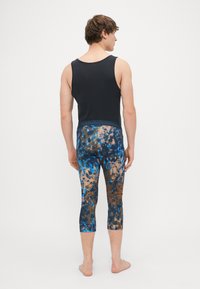 Top de alças preto sem mangas com decote redondo, combinado com leggings capri justas apresentando um padrão tie-dye multicolorido em azul e castanho.