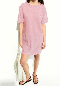 Czerwona i biała sukienka koszulowa w paski, z krótkimi rękawami, okrągłym dekoltem oraz kieszonką na piersi. W zestawie z czarnymi sandałami i lekką kurtką.