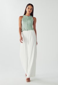 Top senza maniche verde menta con zip frontale, abbinato a pantaloni bianchi a gamba larga. Tessuto dalla texture liscia, design minimalista.