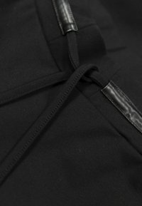 Textile noir avec une surface lisse, arborant un détail de nœud central et des accents noirs brillants. Le tissu semble élastique et mat.