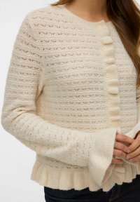 Krämfärgad stickad kofta med diskreta horisontella ränder, rund halsringning, knäppning fram, ribbade ärmslut och volangkant nederst.