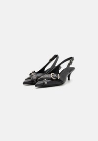 Sapatos de salto slingback pretos com biqueira pontiaguda, apresentando uma tira larga com metal prateado e tachas decorativas. Material em couro liso e salto de altura média.