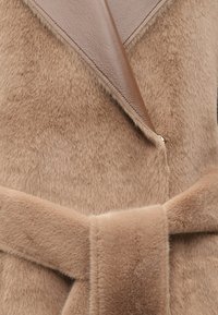 Rudas dirbtinio kailio paltas su odiniu apykakle, turintis platų apykaklę ir surišamą diržą liemens. Minkšta tekstūra ir šilta spalva.