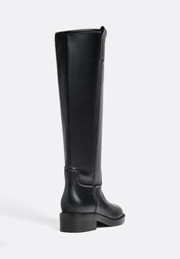 Alti stivali in pelle nera con una texture liscia, punta arrotondata e tacco basso a blocco; presentano una cucitura lungo il lato esterno e un elastico per indossarli.
