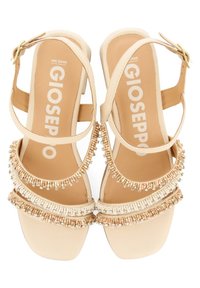 Sandales à talon beige avec un talon bloc, dotées de plusieurs brides perlées et d'une boucle à la cheville à l'arrière. Texture lisse avec des accents décoratifs.