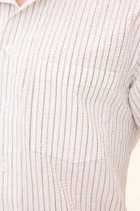Gros plan d'une chemise blanche à boutons avec des fines rayures verticales marron et noires et une poche poitrine du côté gauche.