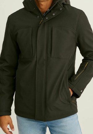 Mand iført en mørkegrøn hættetrøje med lynlås og trykknapper, lynlåslomme på ærmet og to forlommer, kombineret med lyseblå jeans.