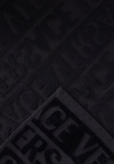 Tissu texturé foncé avec des lettres en relief formant des mots dans un motif en grille, mettant en valeur le contraste entre les zones noires mates et brillantes.