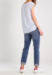 Camicia a righe blu e bianche con maniche corte abbinata a jeans blu scuro con risvolti e sneakers bianche con dettagli rossi.