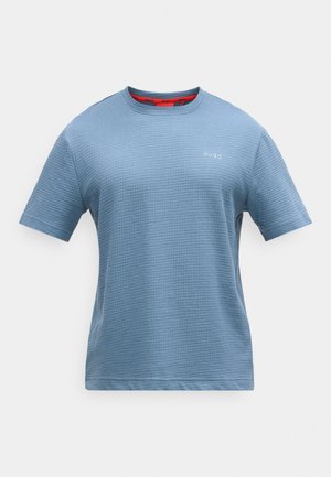 Kortermet blå t-skjorte laget av strukturert stoff. Har rund hals med rød innside, og en liten hvit logo på brystet.