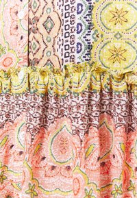 Tissu à motifs colorés avec des designs floraux corail, verts et jaunes, alternant des imprimés géométriques et une finition à volants.