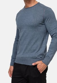 Dunkelblauer Rundhalsausschnitt-Pullover aus weichem Strickstoff. Verfügt über lange Ärmel und gerippte Bündchen. Minimales Logo-Detail nahe dem Saum.