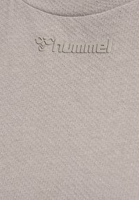 Close-up van lichtgrijze gestructureerde stof met verhoogd "hummel" merklogo en bijen symbool nabij een kraag.