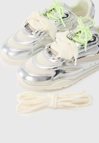 Ασημί αθλητικά παπούτσια με διάτρητο και υφασμάτινο υλικό, με πράσινα και κρεμ κορδόνια και διακριτικό λογότυπο. Περιλαμβάνει επιπλέον ζευγάρι κρεμ κορδόνια.