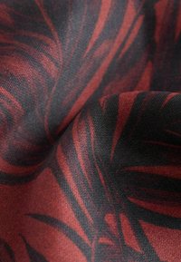 Tissu présentant un fond dense et sombre avec de grands motifs de feuilles rouges et noires en tourbillon. Le tissu a une texture douce et mate.