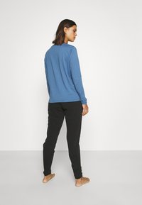 Top azul de manga larga con cuello redondo, combinado con pantalones de chándal negros ajustados. Textura suave, diseño ceñido y estilo minimalista.