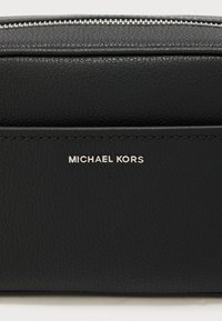 Μαύρο δερμάτινο πορτοφολάκι με υφή στην επιφάνεια, που διαθέτει ασημί φερμουάρ και ανάγλυφο λογότυπο "MICHAEL KORS" στο μπροστινό μέρος.