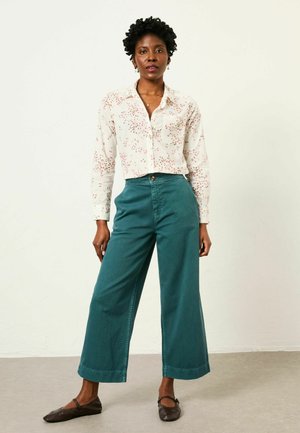 White long-sleeve shirt with red floral pattern, paired with high-waisted teal wide-leg pants. Brown flat shoes complete the outfit.