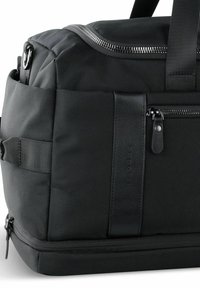 Sac de sport noir en nylon texturé, avec une finition en cuir lisse, des compartiments zippés et deux poignées robustes.