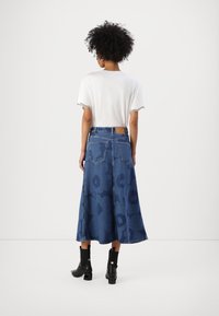 Denim maxi szoknya nagy virágmintákkal, különböző kék árnyalatokban, fehér rövid ujjú inggel és fekete bokacsizmával párosítva.